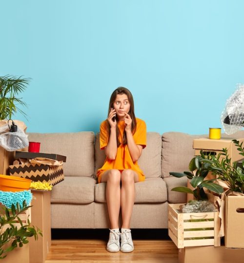 photo-serious-woman-calls-someone-via-smartphone-sits-comfortable-sofa-shares-news-about-buying-new-apartment-surrounded-with-personal-belongings-relaxes-new-home-moving-concept_273609-30600