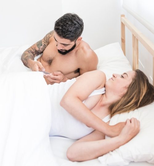 woman-lying-bed-looking-her-husband-using-smartphone_23-2147911936